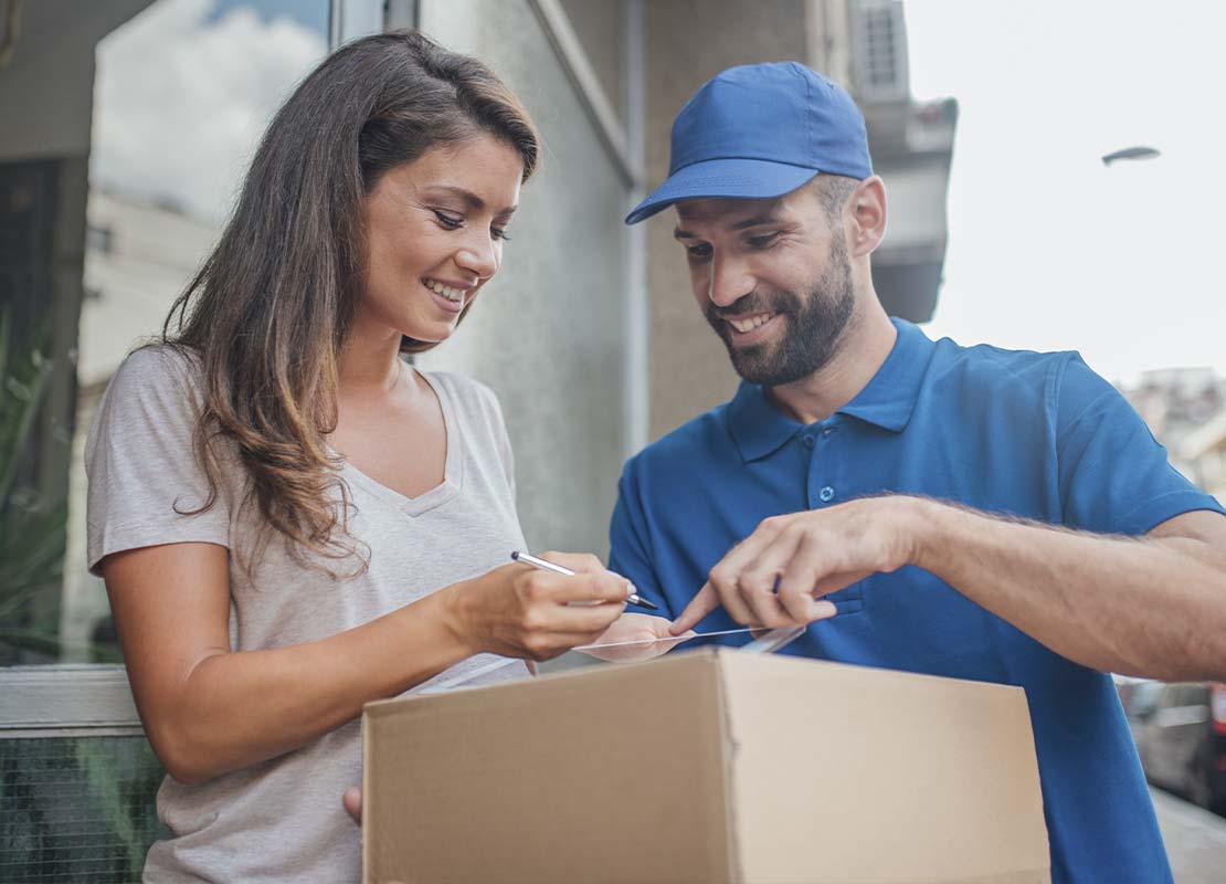 Mujer firma en Tablet confirmando la recepción de una caja con alimentos que entrega un domiciliario