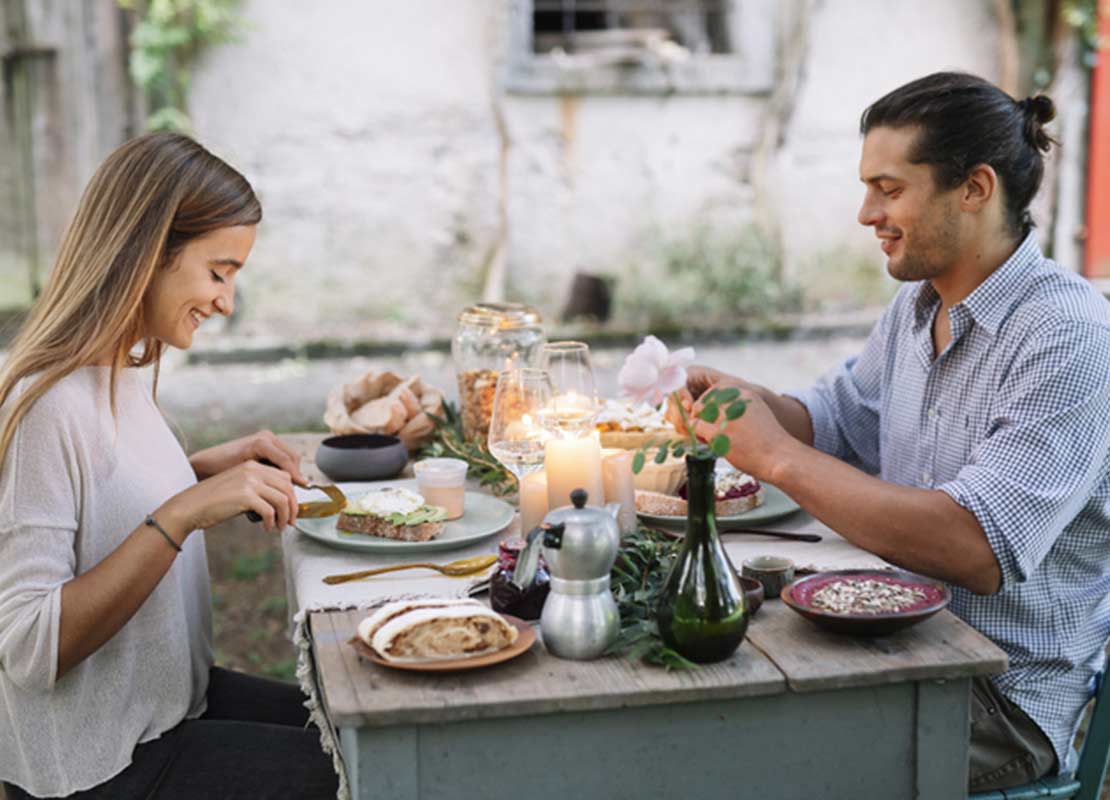 Fuera de un restaurante, pareja sentada a la mesa corta los alimentos al frente de ellos
