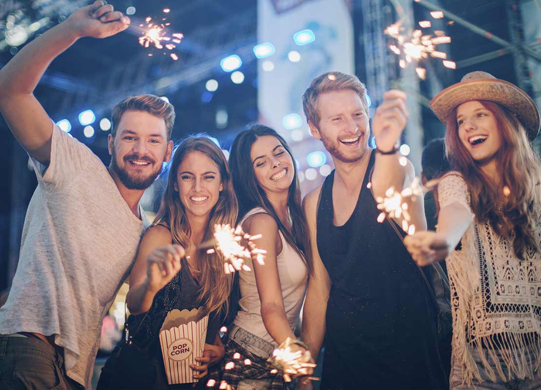 Amigos celebran con pequeñas chispas de fuegos artificiales en sus manos y una de ellas sostiene pop corn
