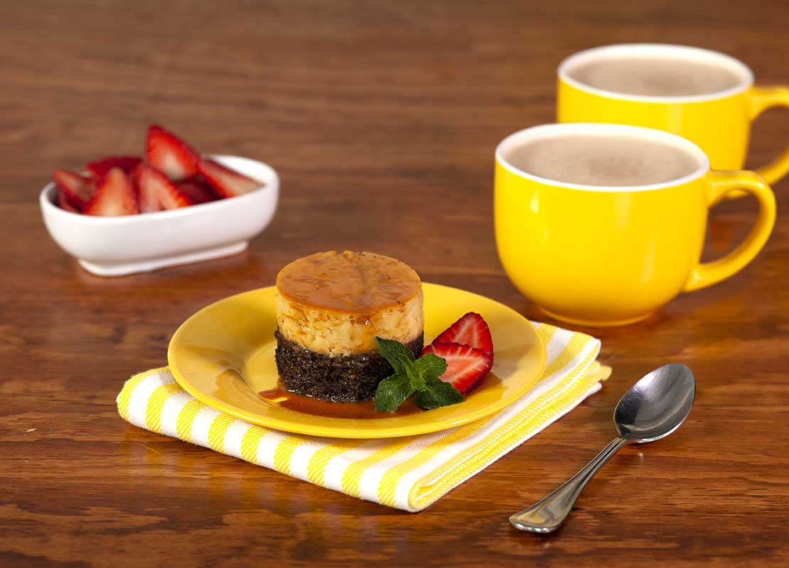 Mini chocoflan decorado con fresas y hierbabuena, al lado dos tazas amarillas de chocolate caliente