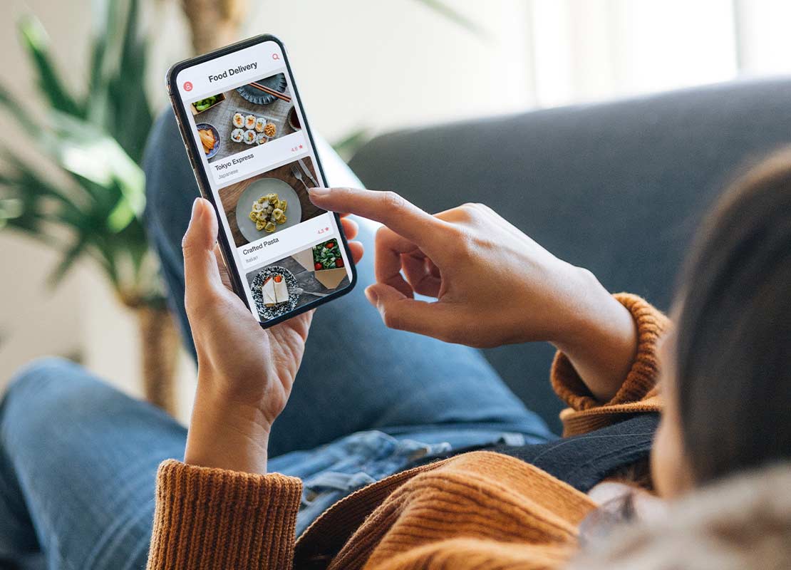 Mujer recostada en un sofá revisa el menú digital de un negocio de food service desde su celular