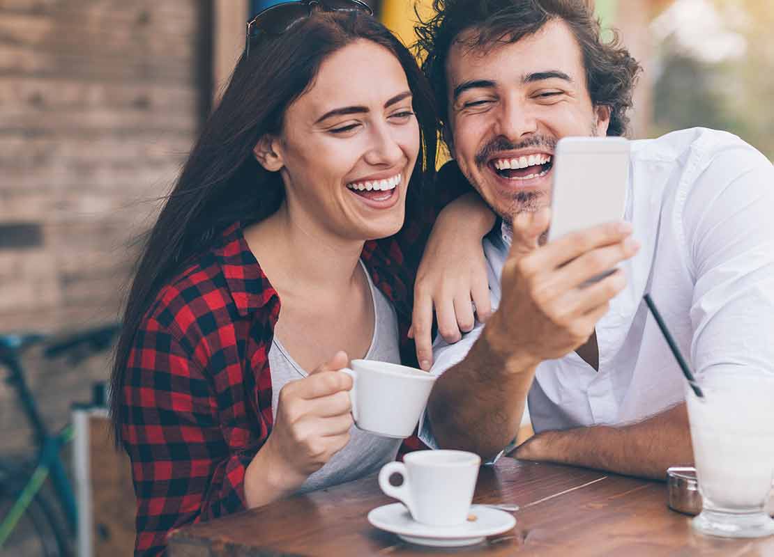 Pareja sentada a la mesa se toma una selfie mientras bebe café a las afueras de una cafetería