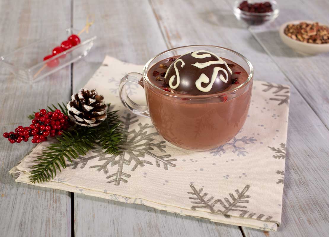 Taza de cristal con bebida caliente y una bomba de chocolate, al lado, decoraciones navideñas