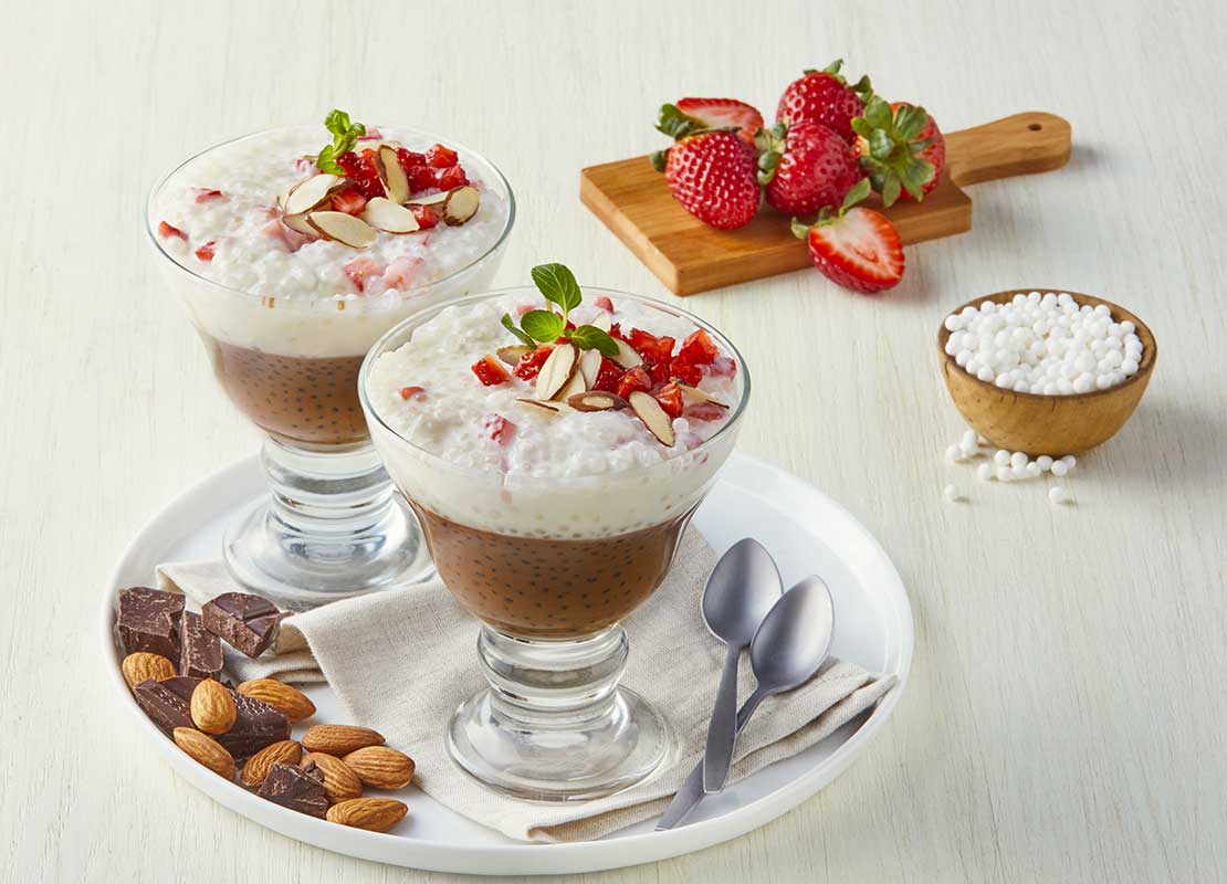 2 copas de gelatina, tapioca, crema y láminas de fresa en un plato con frutos secos y trozos de chocolate