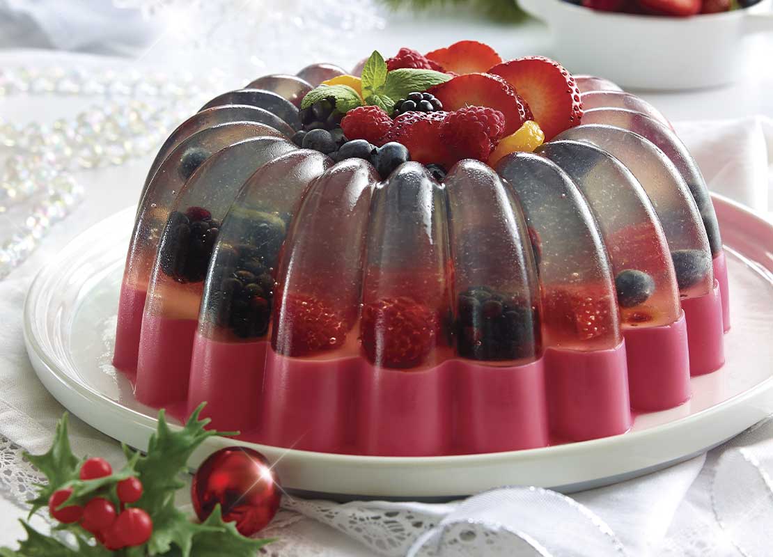 Gelatina desmoldada bicolor, rellena de fruta y decorada con trozos de fresa, mora y arándanos
