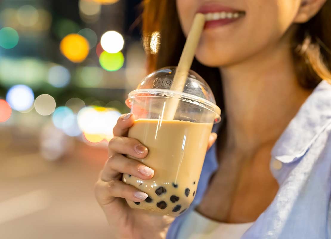 Mujer bebe un bubble tea en un vaso plástico con pajilla y con perlas al fondo que sostiene en su mano