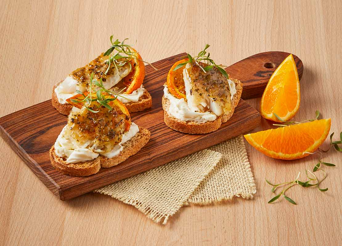 3 canapés de pan, crema y naranja servidos sobre una tabla de picar