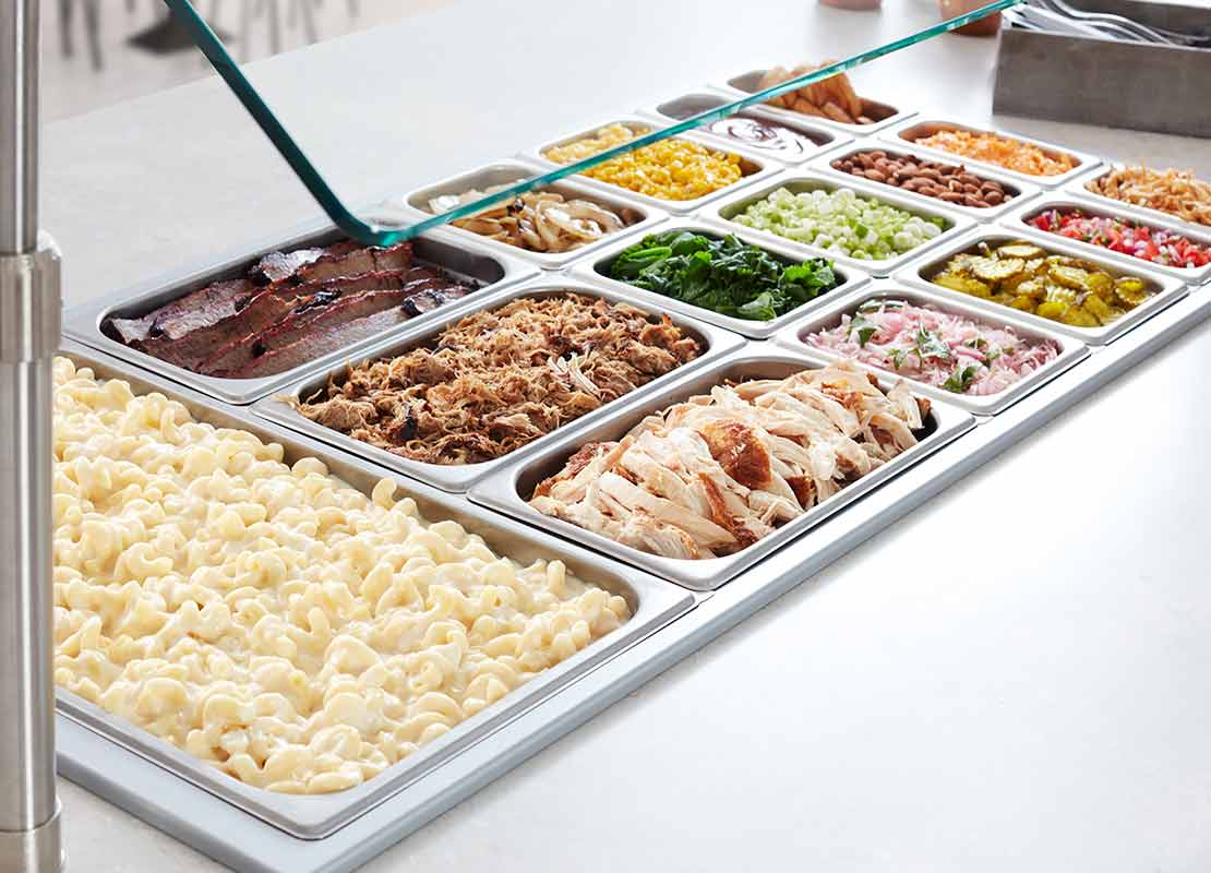 Mesa de buffet de contenedores con proteínas, pasta, verduras, frutas y ensaladas