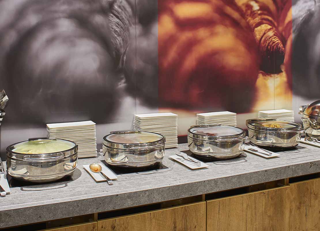 Mesa de buffet con ollas que contienen diferentes alimentos, utensilios, servilletas, platos y pocillos
