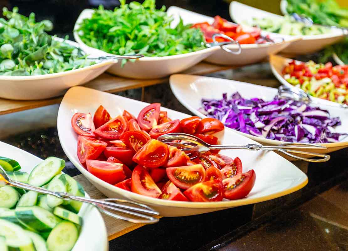 Mesa de buffet con diferentes tipos de verduras y ensaladas servidas en tazones blancos