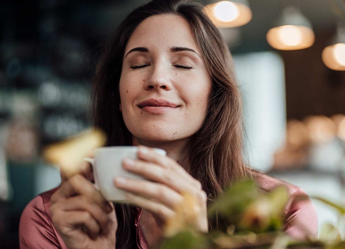 Mujer sostiene una taza de café frente a ella mientras disfruta de su aroma en una cafetería