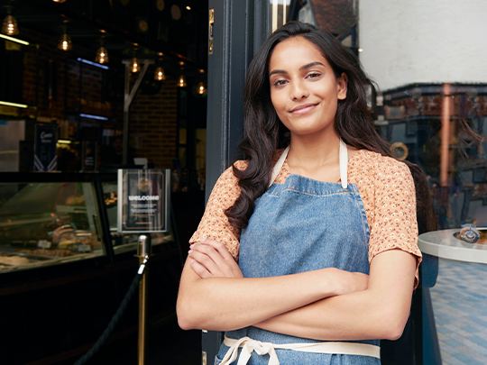 Persona  de pie y con los brazos cruzados a la entrada de una cafetería.