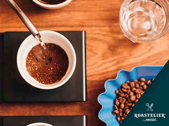 Agua caliente en una taza de café con un plato de granos de café sobre una mesa de madera.