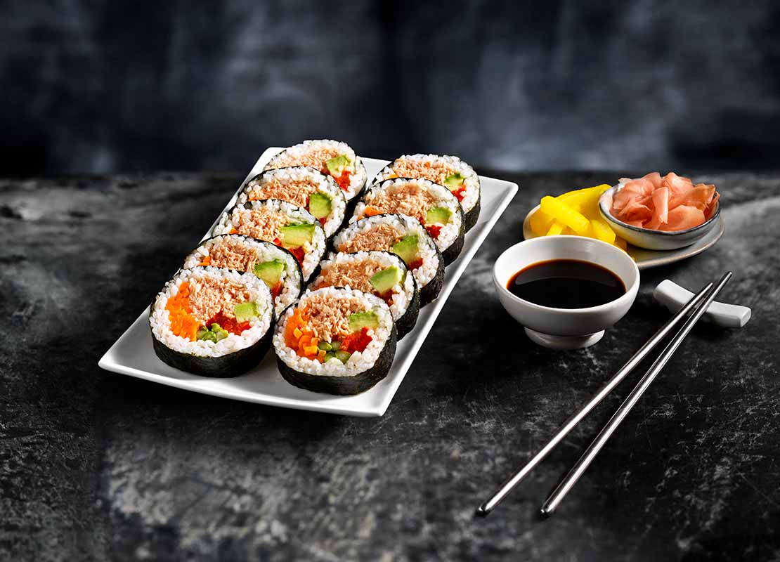 10 piezas de sushi en un plato, al lado salsa de soya, jengibre y palillos chinos sobre un soporte