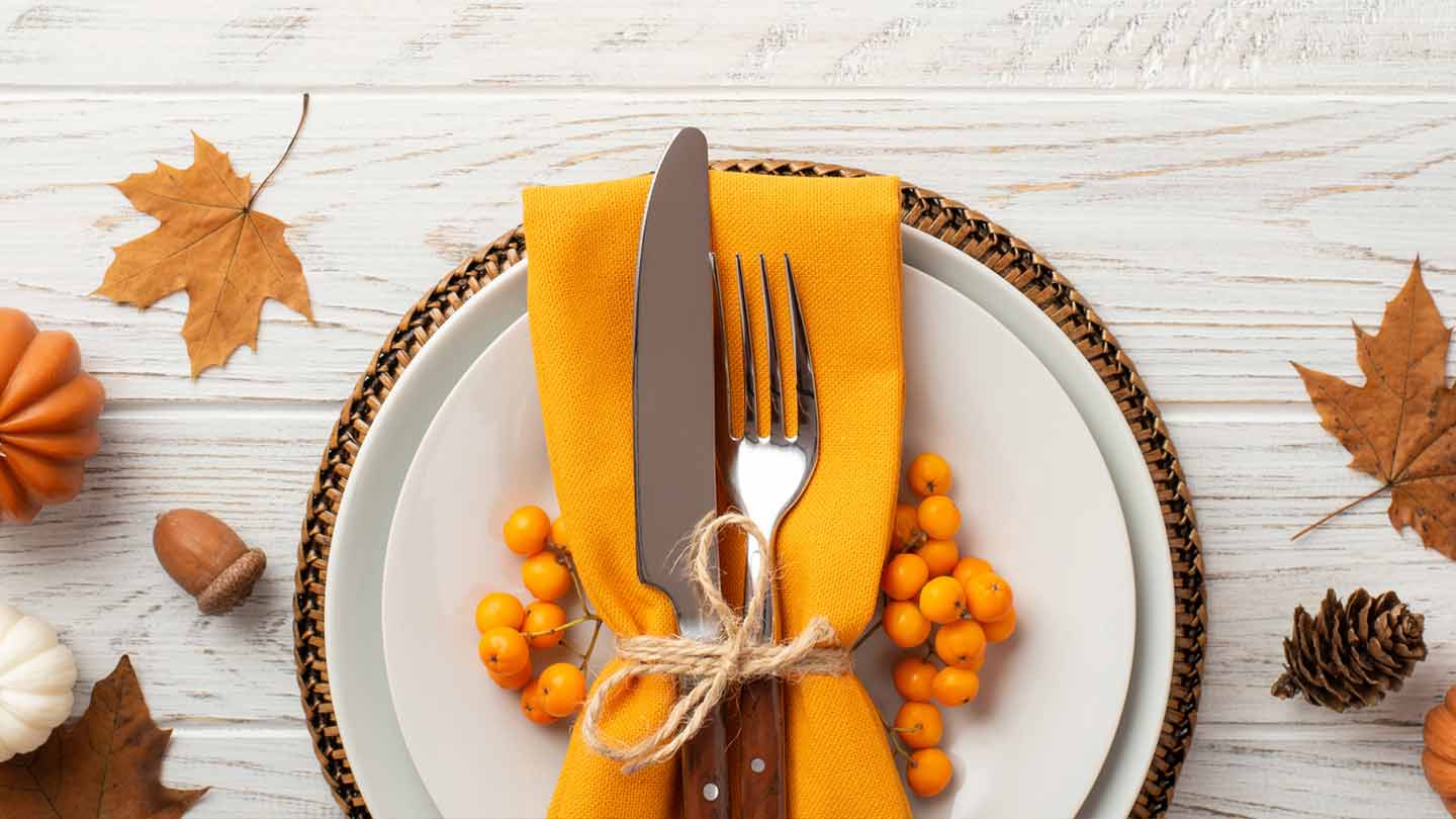 Tenedor y cuchillo atados a una servilleta naranja sobre un plato, alrededor decoraciones de otoño