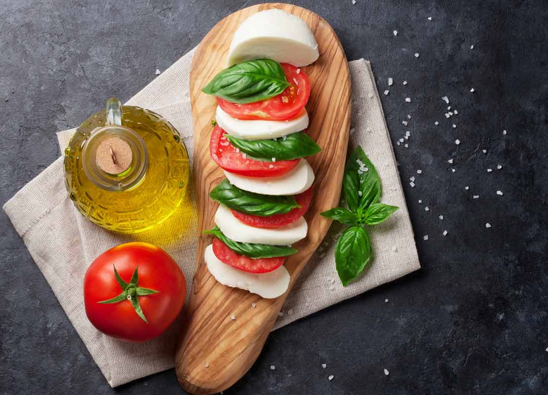 Ensalada caprese sobre una tabla de madera, ejemplo de tipos de corte en la cocina, con albahaca, tomate y mozzarella
