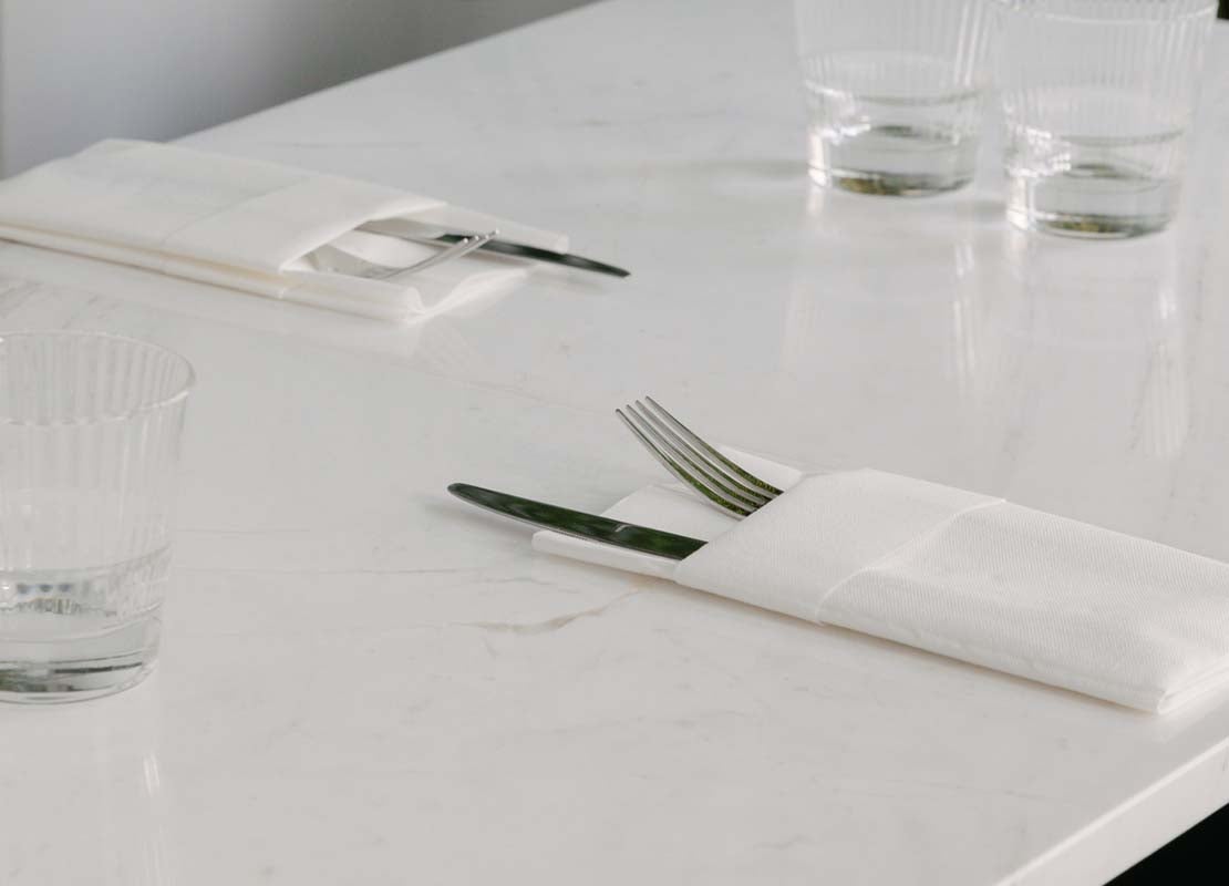 Mesa minimalista con cubiertos en servilletas blancas, destacando cubiertos formales