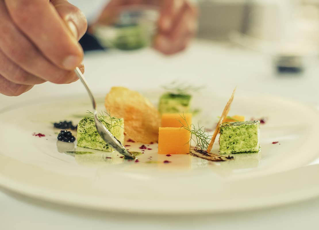 Manos de chef decoran con una cuchara, realizando un emplatado sofisticado para un restaurante gourmet