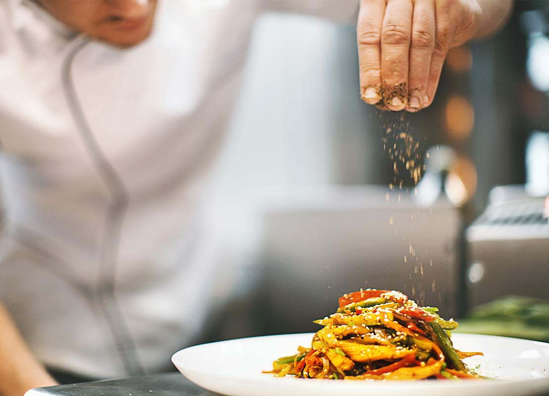 En una cocina de un cliente, chef finaliza un platillo agregando una pizca de especias