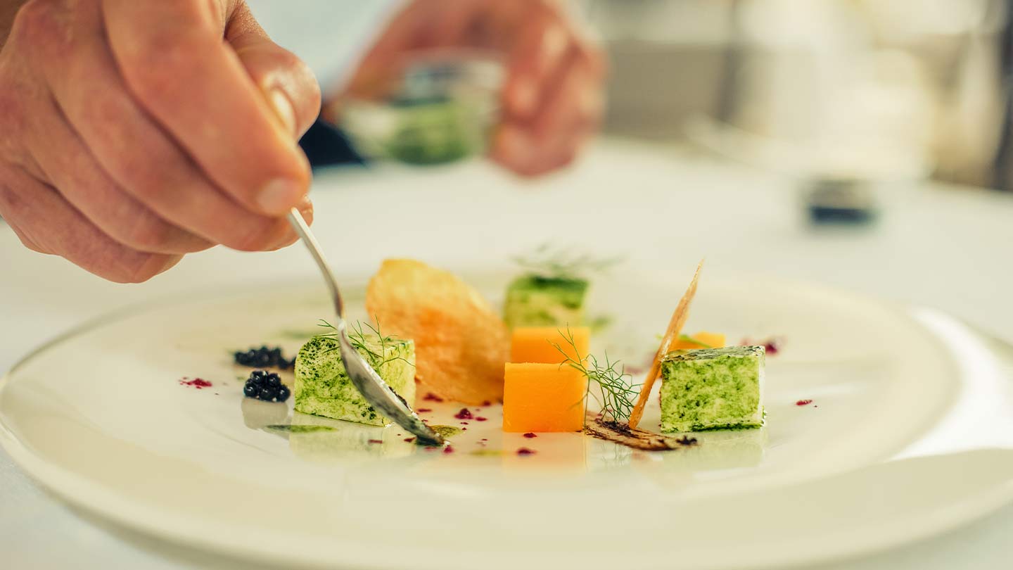 Mano de chef decora con aderezo un plato blanco de vegetales en cubos