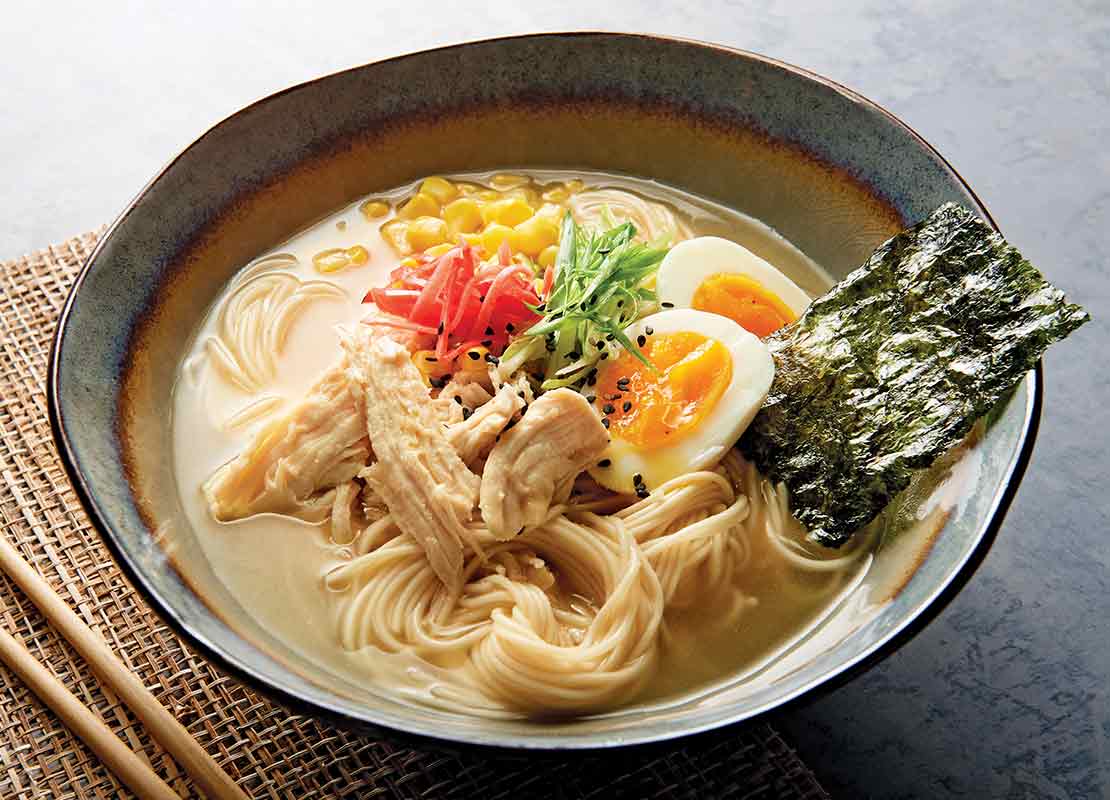 Plato de ramen con toppings como huevos cocidos, algas, maíz, pollo desmenuzado y vegetales