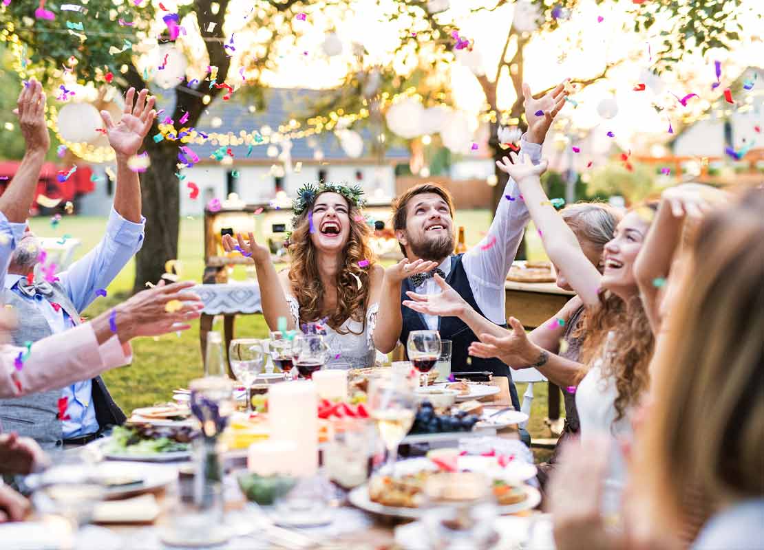 Pareja al final de una mesa larga con comida servida celebra su matrimonio, al rededor otros invitados