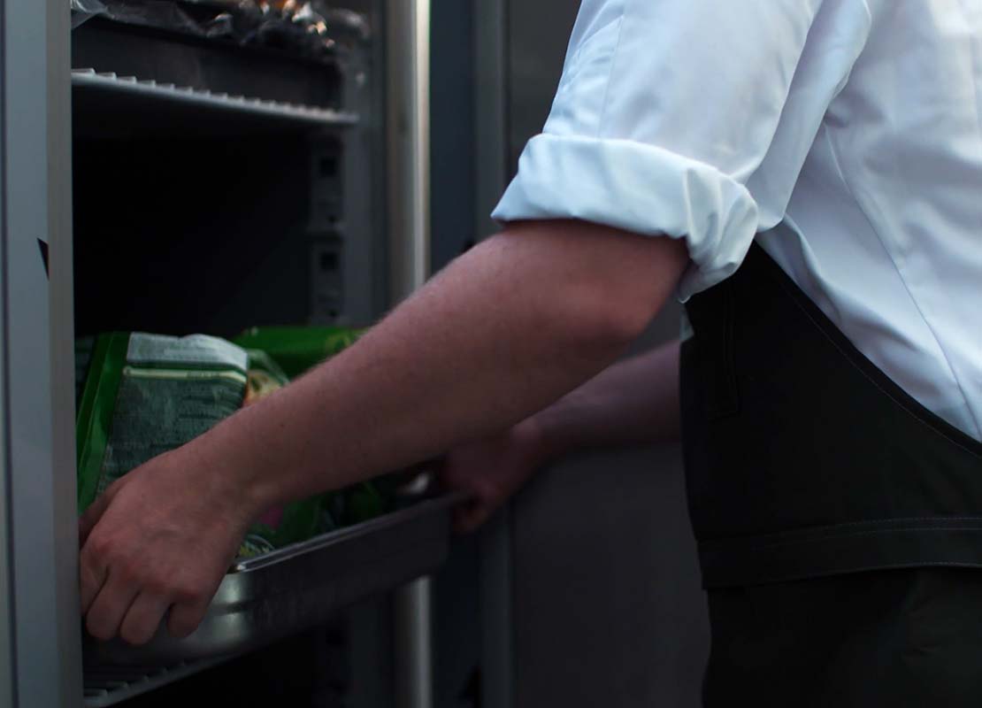 Ayudante de cocina retira una bandeja con alimentos refrigerados de un congelador industrial