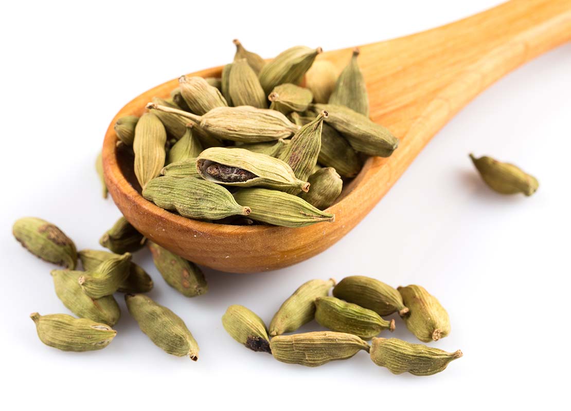 Cuchara de palo con vainas de cardamomo seco que pasaron por un proceso de deshidratación