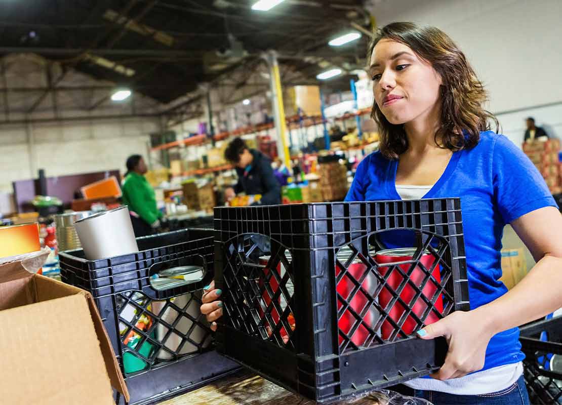 En una bodega, trabajadora mueve cajas con productos de alimentos para apilarlas