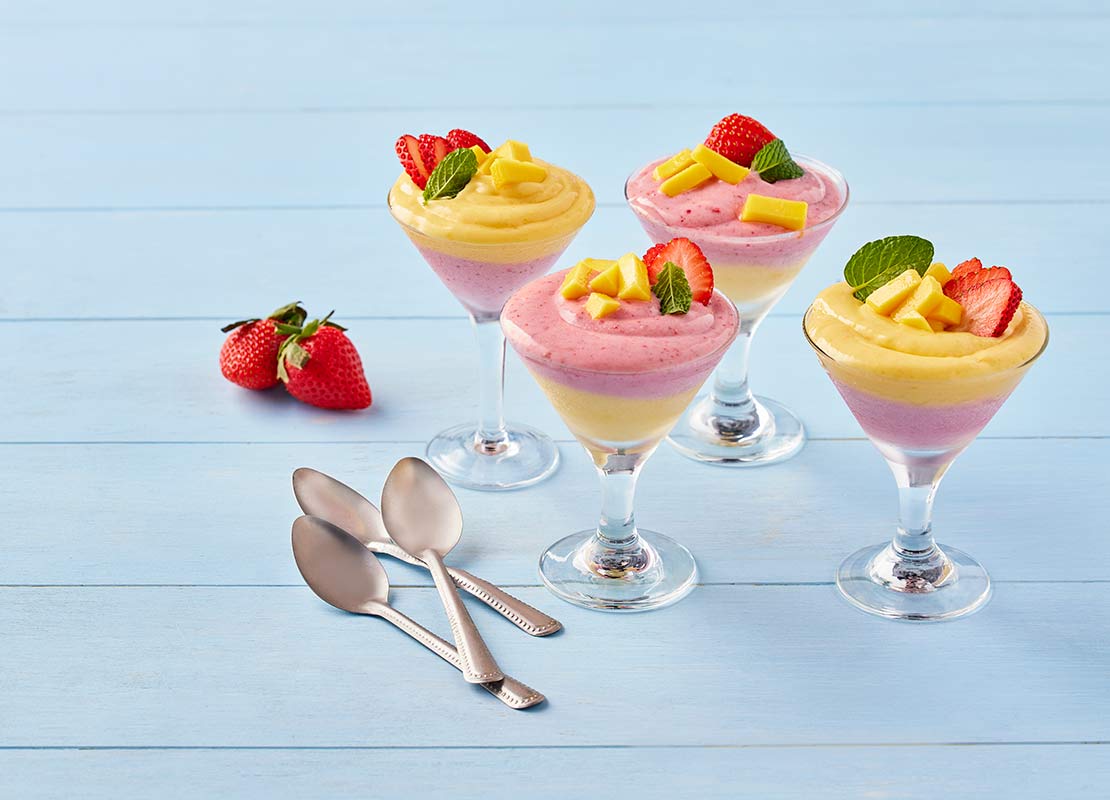 4 copas de mousse de mango y fresa decorados con fruta y hojas de hierbabuena