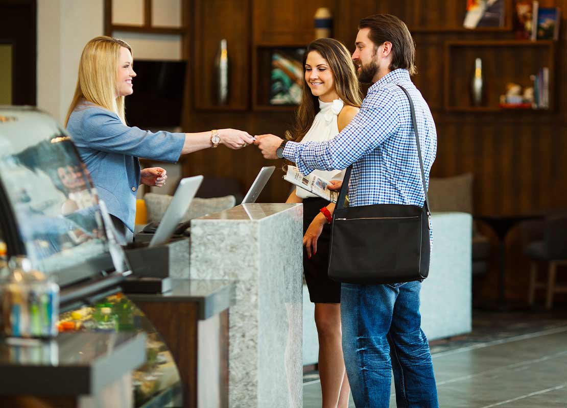 Recepcionista registra en un portátil el pago de dos huéspedes en un hotel