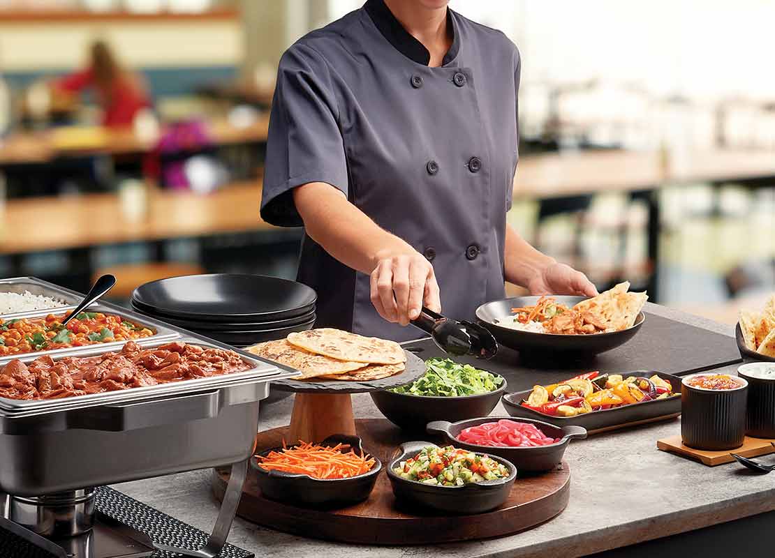 Chef sirve comida en un buffet con una variedad de platillos en un entorno de restaurante