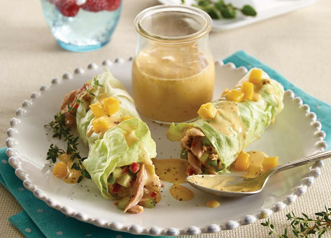 2 wraps de verduras envueltos en lechuda y servidos con aderezo, al fondo agua saborizada y toppings