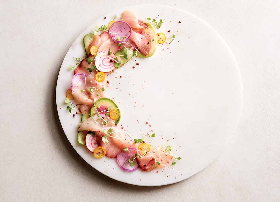 Emplatado de alta cocina de chipotle hamachi crudo con vegetales en un estilo al borde del plato