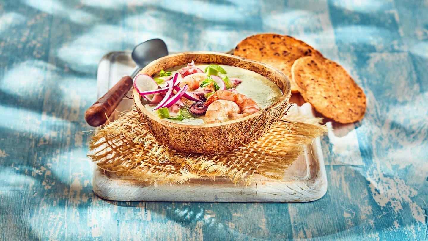 Ceviche de mariscos en cuenco de coco, acompañado de tostadas y decorado con cebolla y hierbas frescas