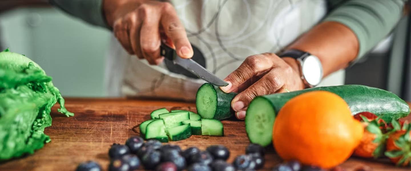 Manos de hombre cortando un pepino junto sobre una tabla de madera