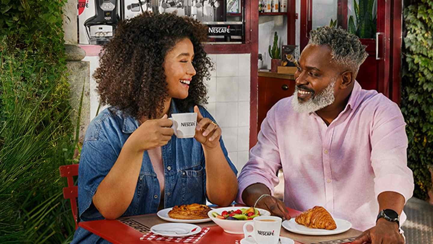 Un hombre y una mujer disfrutan del café NESCAFÉ® y desayuno al aire libre en una terraza