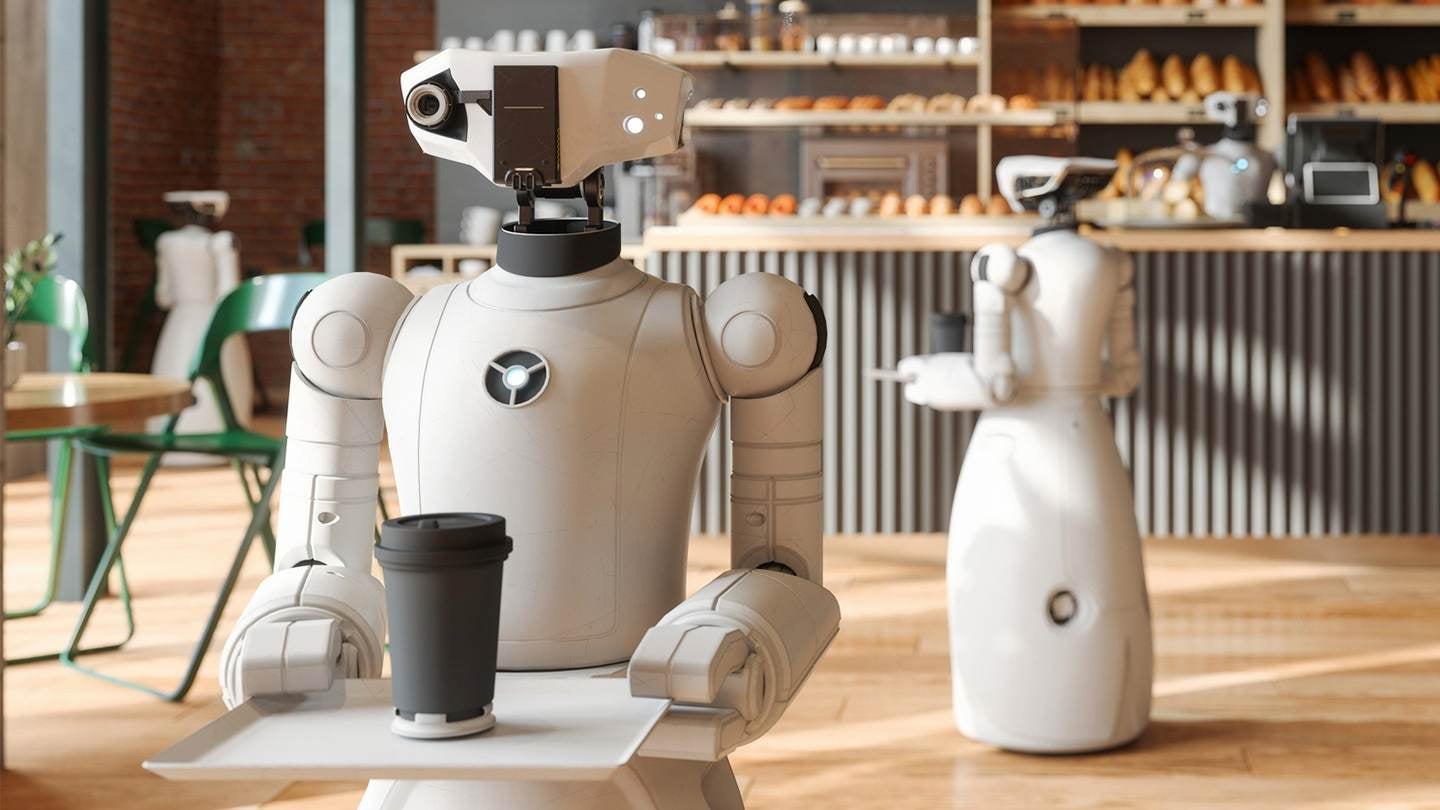 Dos robots recorren una cafetería sosteniendo una bandeja con una bebida caliente con tapa