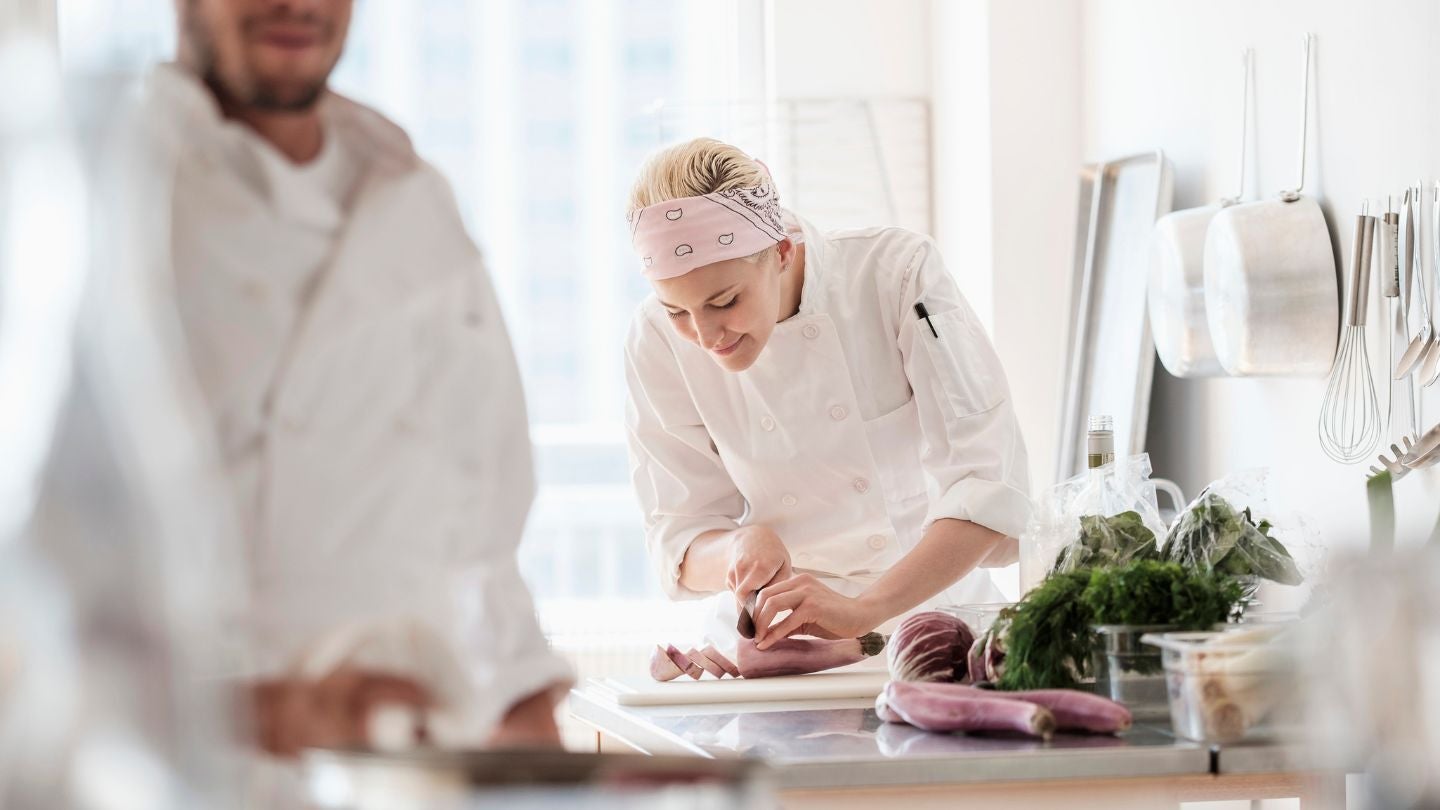 Chef concentrada preparando ingredientes frescos en el área de cocina luminosa de un restaurante.