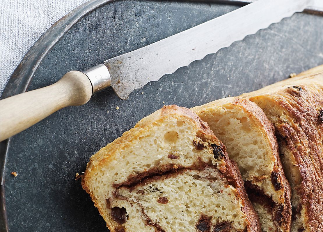 Cuchillo de sierra con mango de madera y un pan de canela y pasas sobre una tabla negra