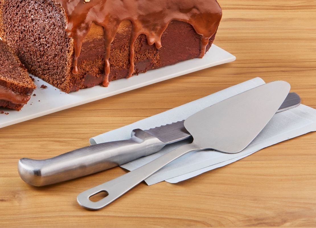 Cuchillo de repostería y pala para servir acompañan un pastel de chocolate sobre una mesa.
