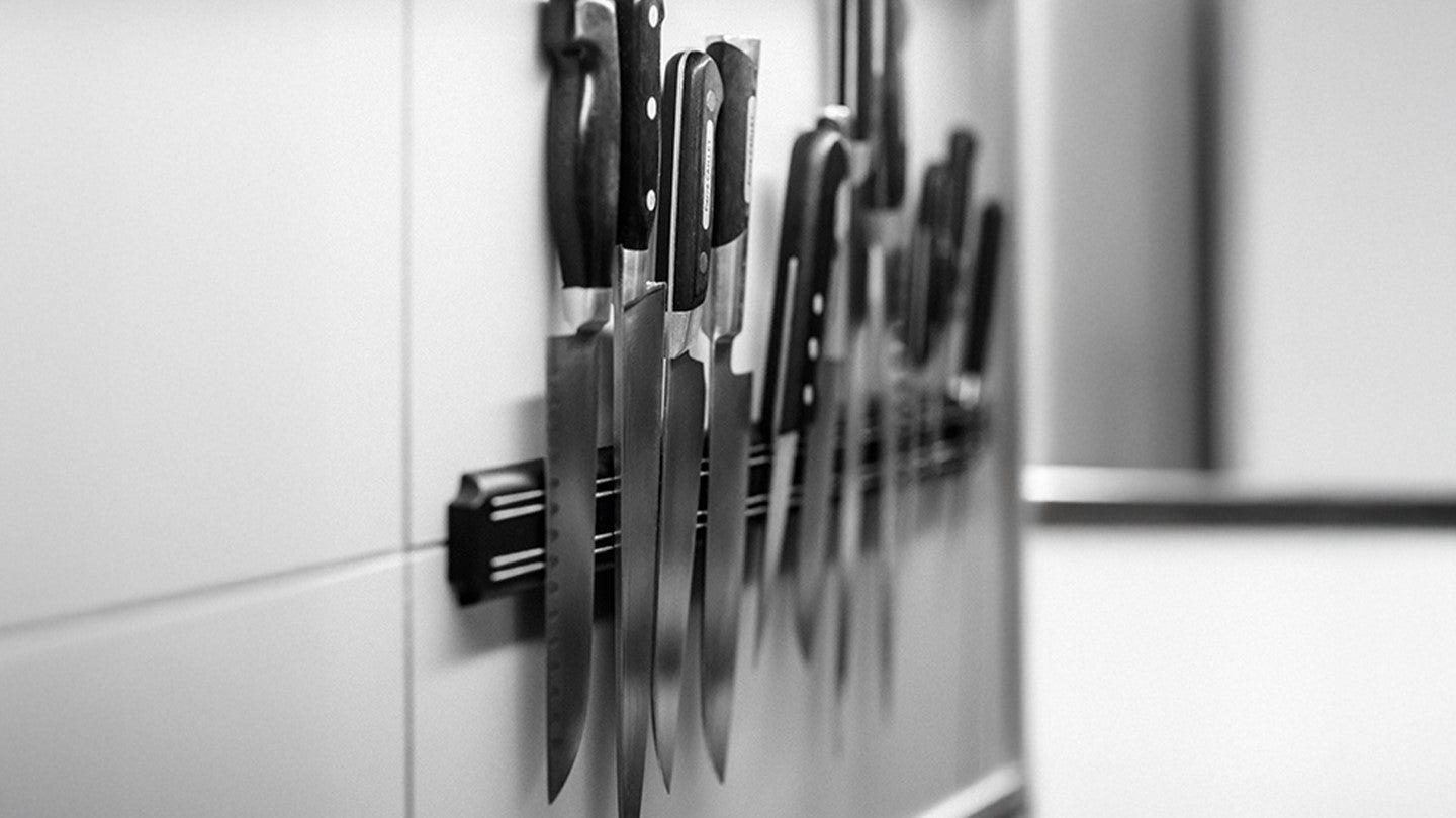 Varios cuchillos de cocina profesionales organizados sobre un soporte magnético en una pared blanca.