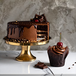 Pastel de chocolate sobre soporte de repostería y un muffing de chocolate acompañando