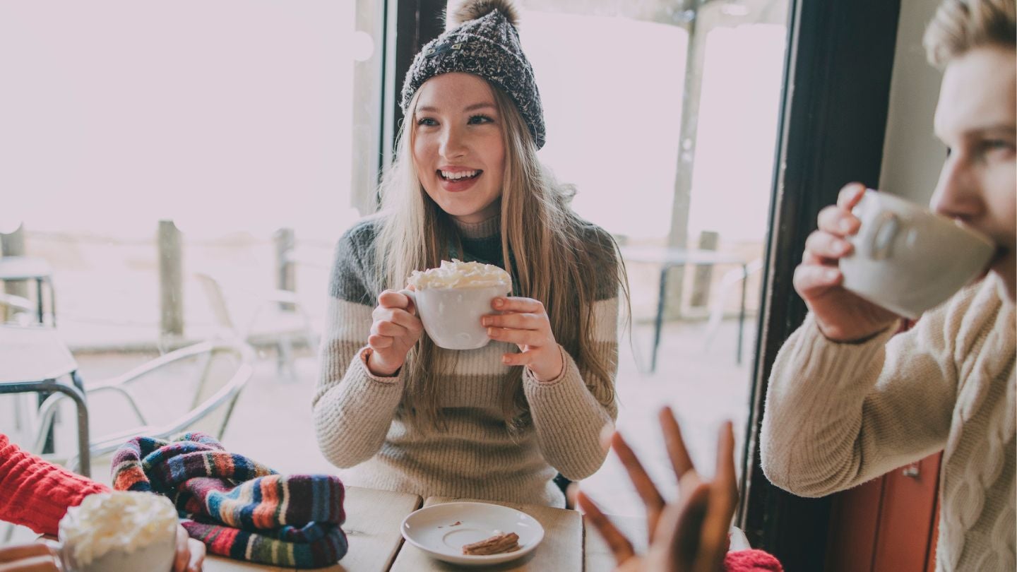 Tres personas bien abrigadas conversan y beben café en la mesa de una cafetería