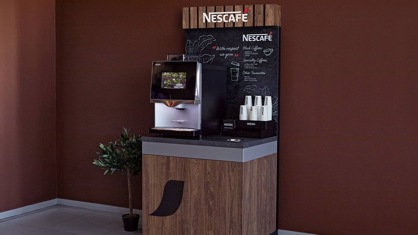 Coffee station de NESCAFÉ con máquina automática y vasos listos para servir bebidas calientes.