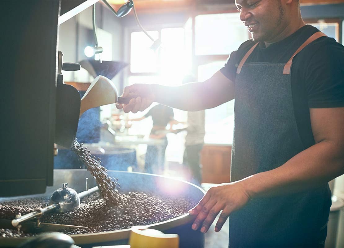 Hombre tuesta granos de café en una máquina tostadora industrial dentro de un almacén