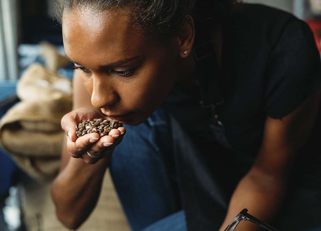 Mujer sostiene un puñado de granos de café tostado mientras disfruta su aroma de cerca