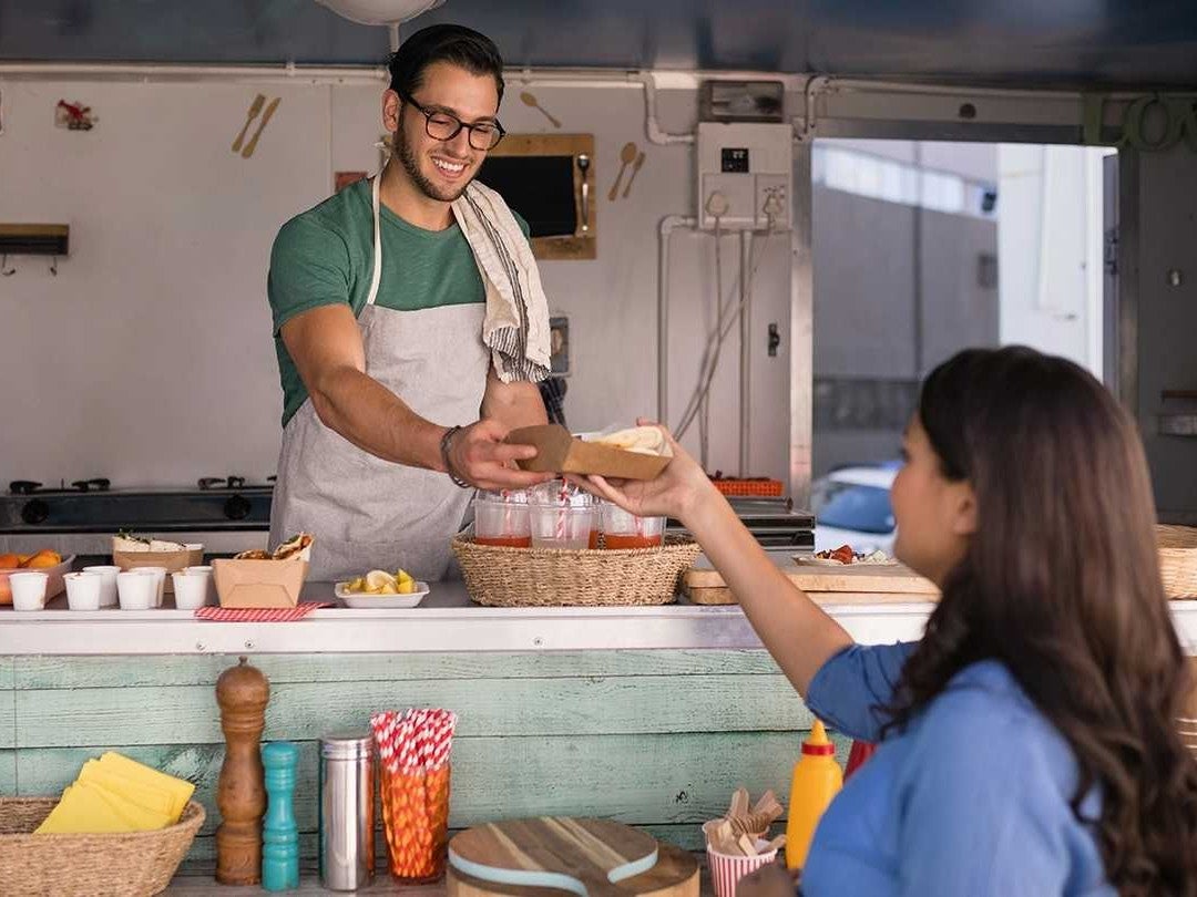 Emprendedor atiende clientes en food trucks ofreciendo comida rápida desde una cocina móvil.
