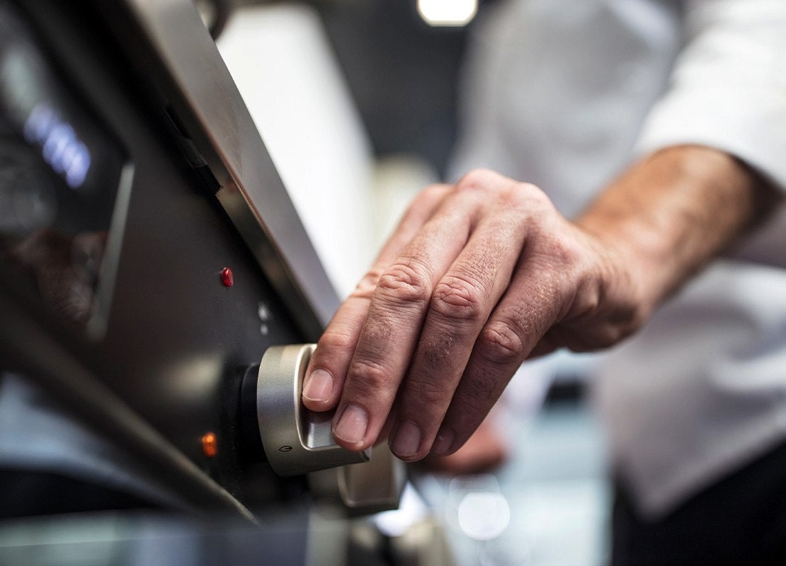 Persona ajusta un control de una estufa durante el mantenimiento de equipos de cocina profesional.