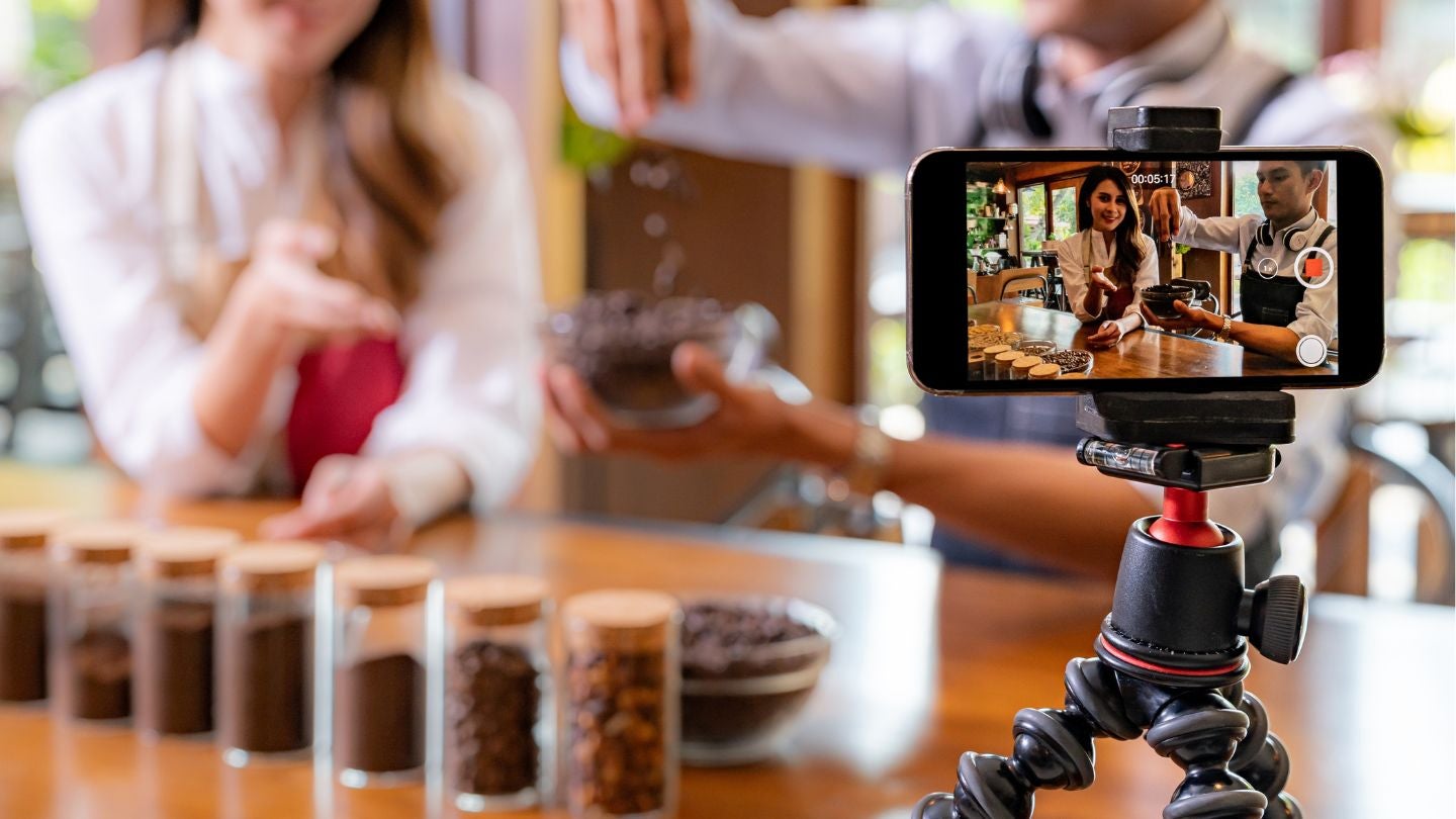 Blogger gastronómico graba contenido sobre café mostrando granos y preparación para redes sociales.